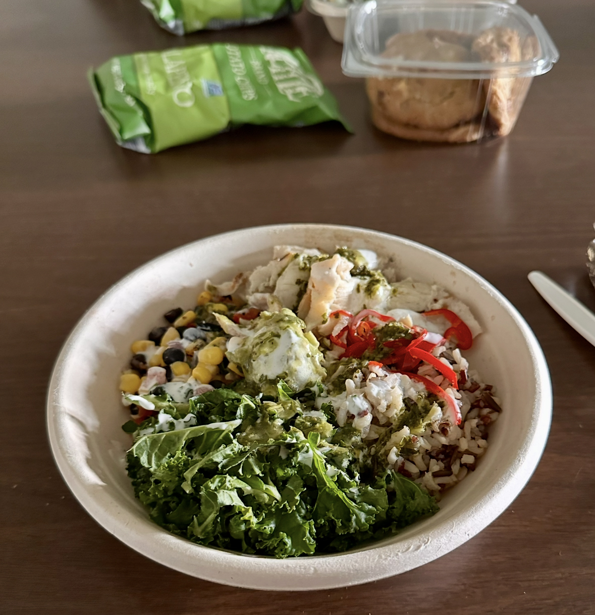 A bowl containing a salad, with chips and cookies to the side.