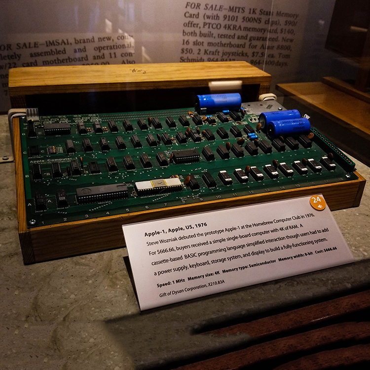 An older-looking computing device (Apple-1) with exposed board, chips, and capacitators.