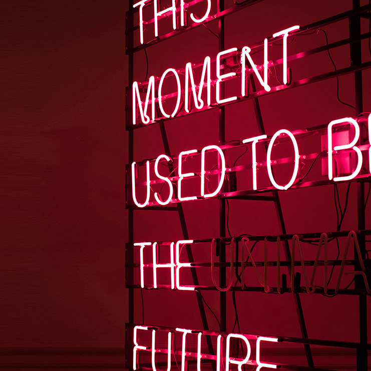 The words 'THIS MOMENT USED TO BE THE FUTURE' are lit up on a frame with a red background.